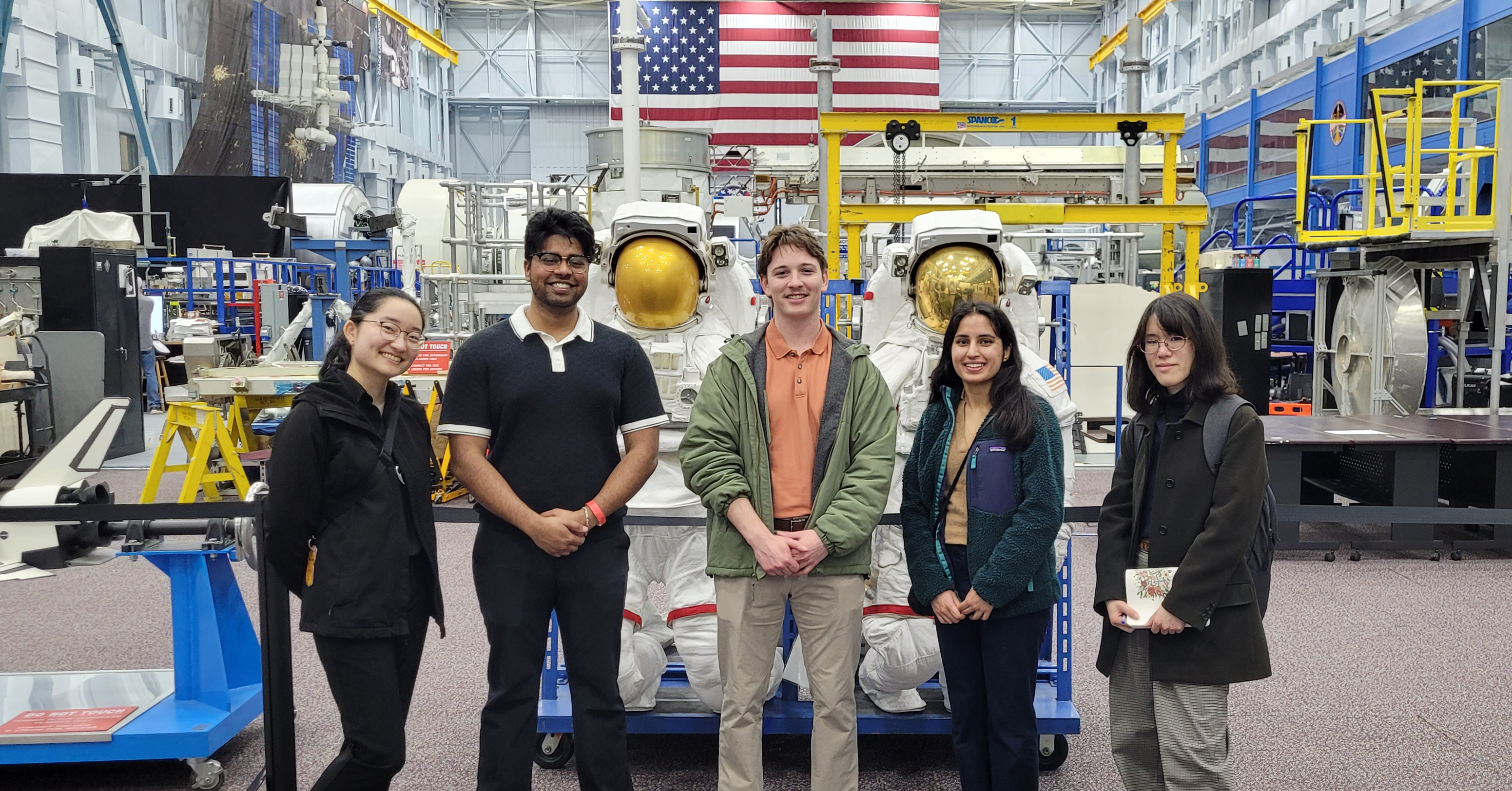 A group of 5 people in front of an astronaut suit