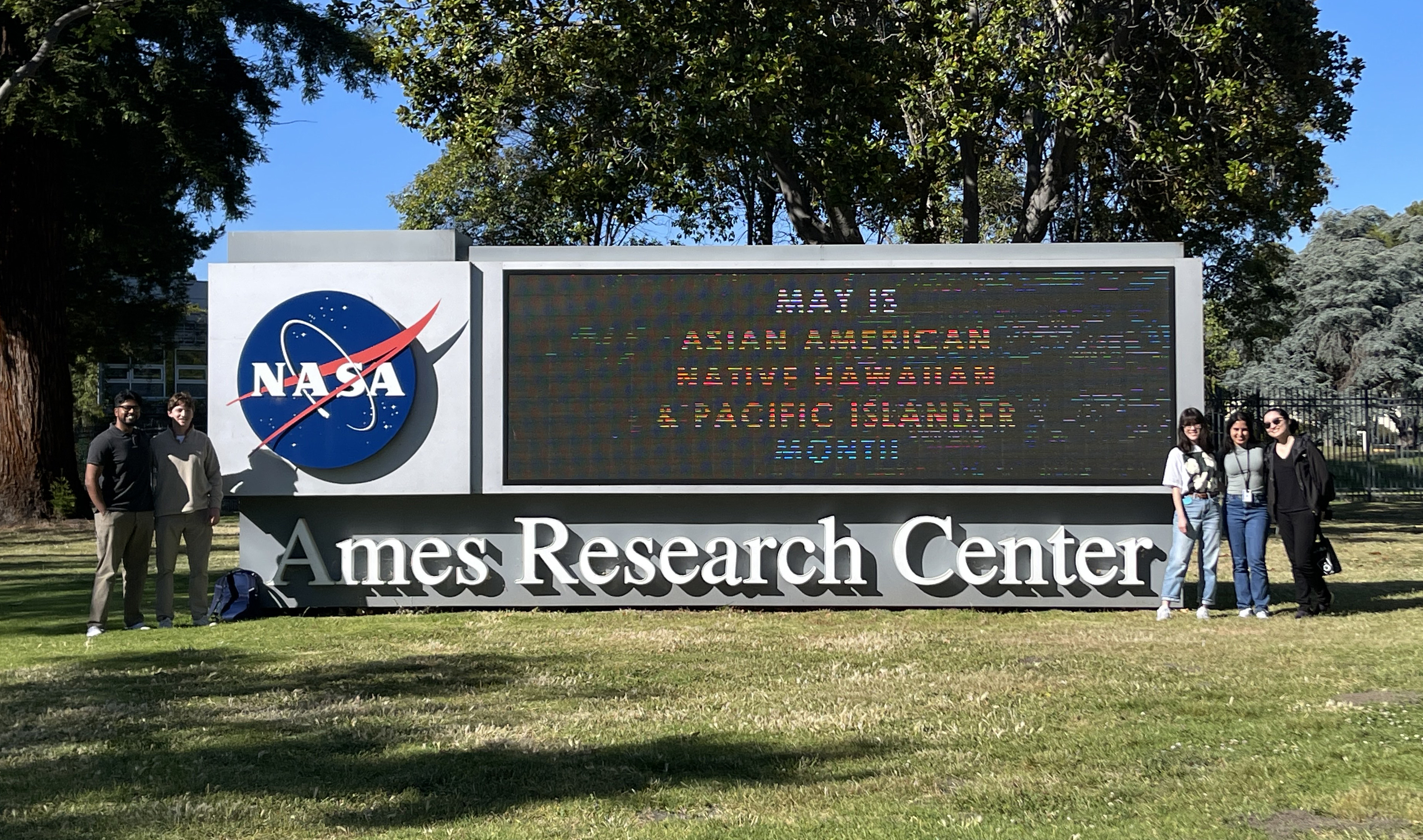 5 people surrounding a NASA sign with 2 people on the left and 3 people on the right